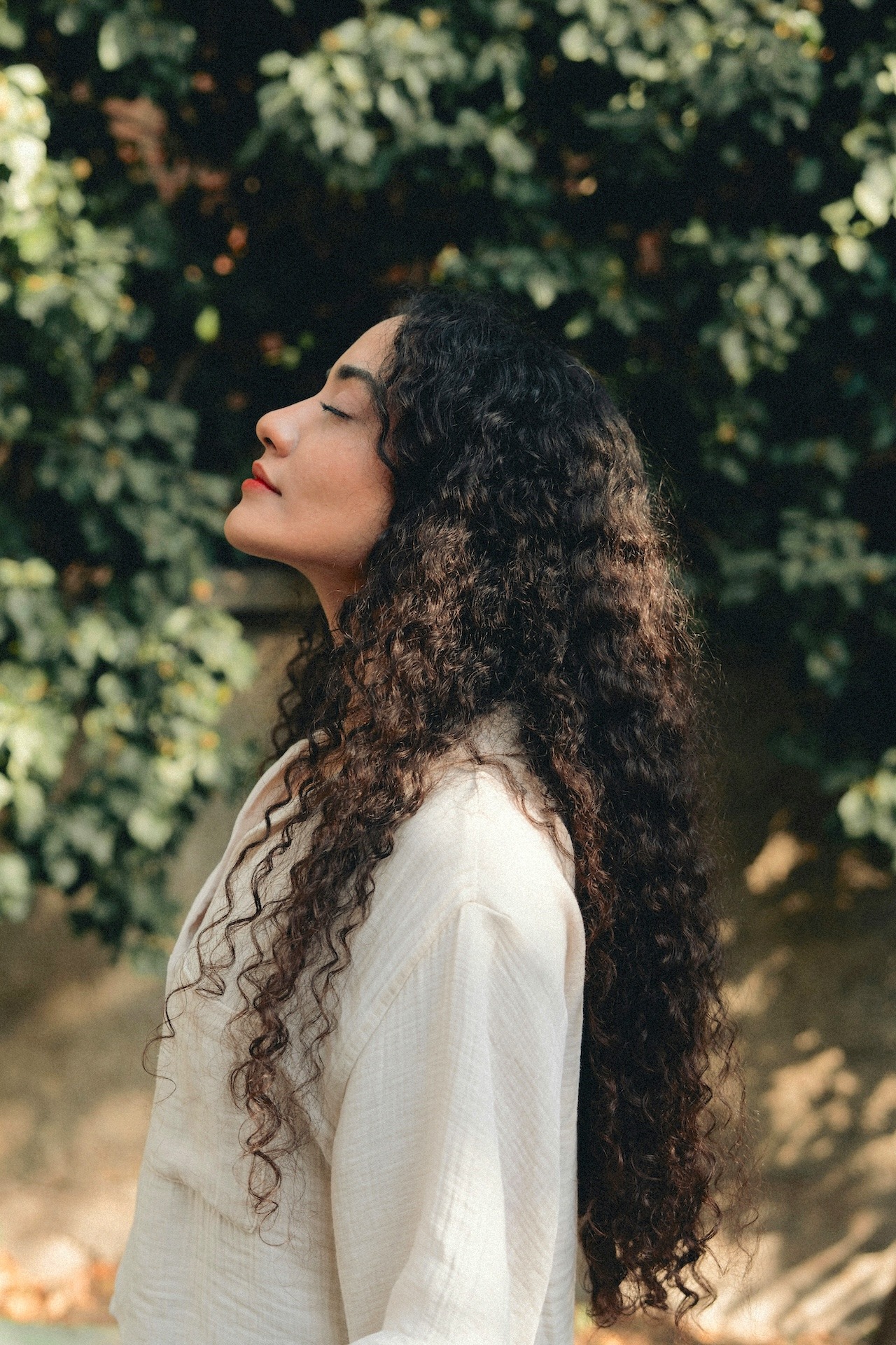 woman looking up with her eyes closed with foliage in the background