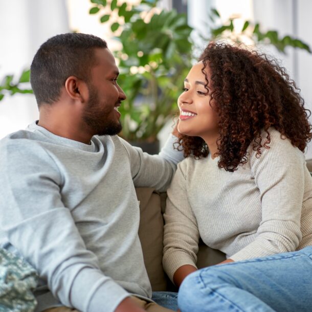 African American couple looking at each other and smiling while sitting on the couch